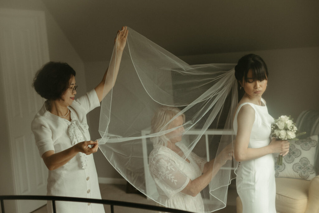 Editorial Styled Wedding Photos of the mother of the bride helping fix the veil while the mother of the groom fixes the dress. Photo taken by a Michigan fine art wedding photographer.