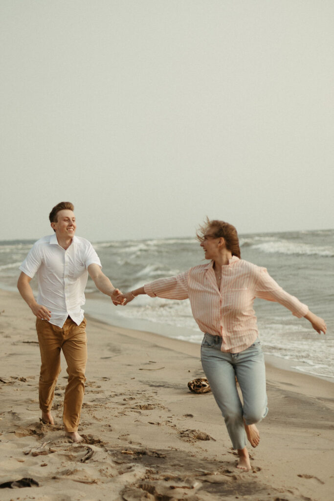 A man and a woman chasing each other around on a beach at lake michigan