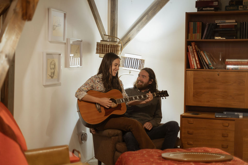 A man and a woman playing music together in a mid century styled air bnb