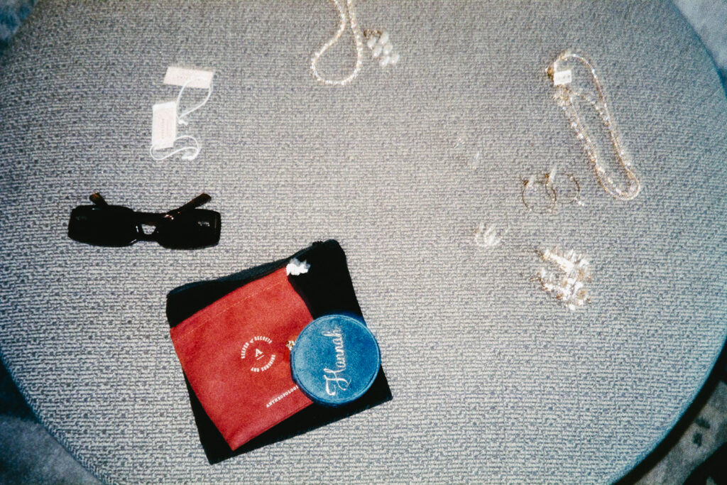 A round table displays various items: sunglasses, jewelry, a red pouch with a smiley face, and a blue patch labeled Heavenly. The surface is textured with a woven pattern.