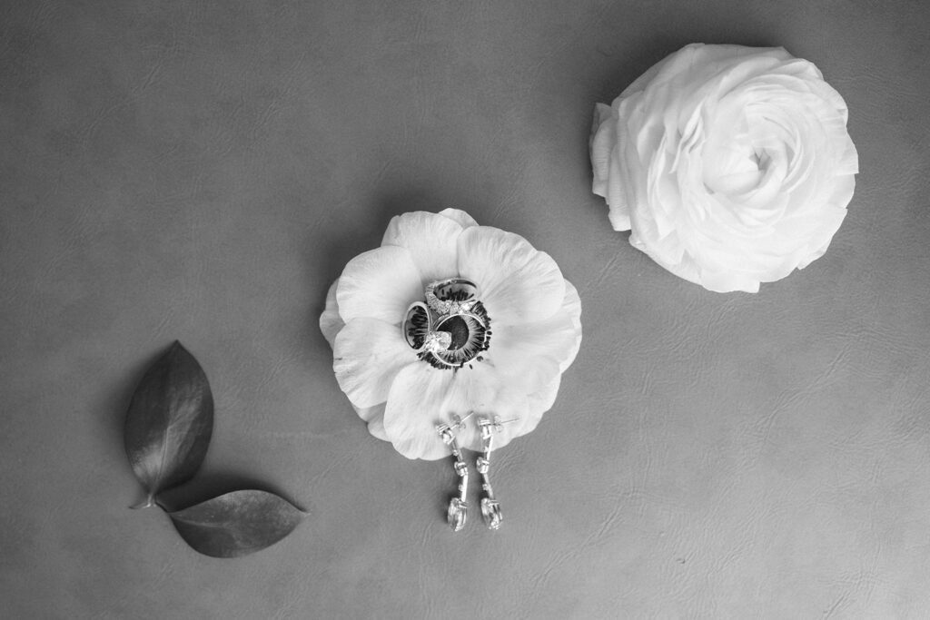 Black and white image of two white flowers on a textured surface, one with a pair of vintage keys resting on its petals. Two dark leaves are placed to the left of the flowers.